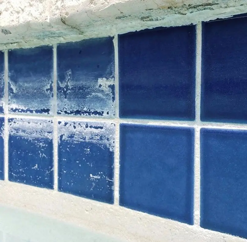 Pool tile with a white calcium scale line, half cleaned